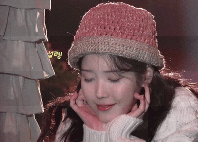 A Woman Wearing A Pink Knitted Hat And A White Sweater Has Her Hands On Her Face GIF