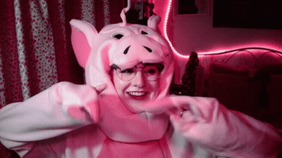 A Woman Wearing A Pink Pig Costume And Glasses Is Smiling . GIF