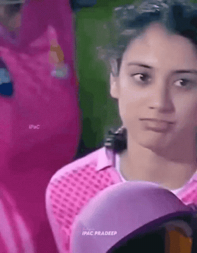 A Woman Wearing A Pink Shirt And A Purple Hat Is Looking At The Camera . GIF