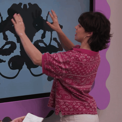 A Woman Wearing A Pink Shirt With A Paisley Pattern Is Touching A Screen GIF