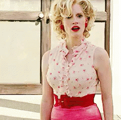 A Woman Wearing A Pink Skirt And A White Top Is Standing In Front Of A Window . GIF