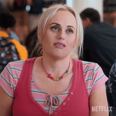 A Woman Wearing A Pink Striped Shirt And A Pink Necklace Is Sitting At A Table . GIF