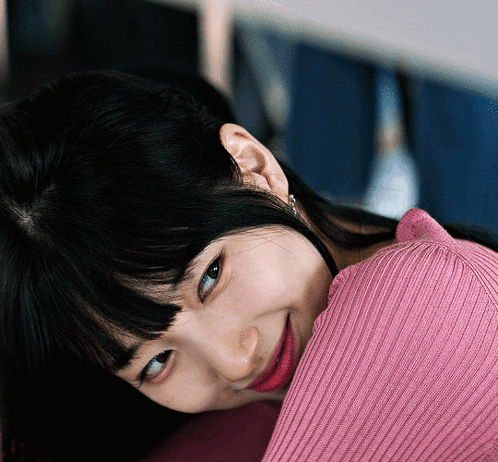 A Woman Wearing A Pink Sweater Is Smiling And Looking At The Camera GIF