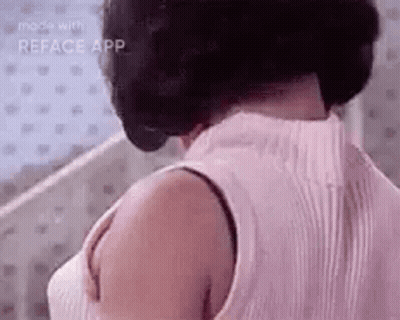 A Woman Wearing A Pink Tank Top And A Bra Is Standing In Front Of A Mirror . GIF
