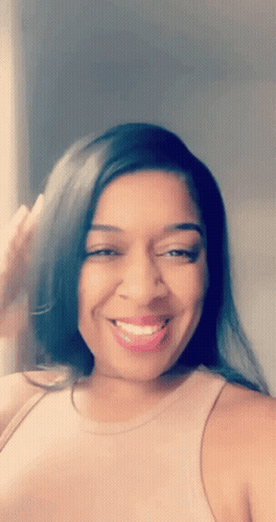 A Woman Wearing A Pink Tank Top Is Smiling And Looking At The Camera GIF