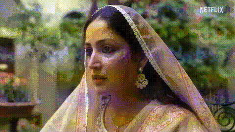 A Woman Wearing A Pink Veil And Earrings Is Looking At Something . GIF