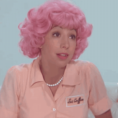 A Woman Wearing A Pink Wig And A Pink Shirt Has A Name Tag On Her Shirt That Says Les Coiffures GIF