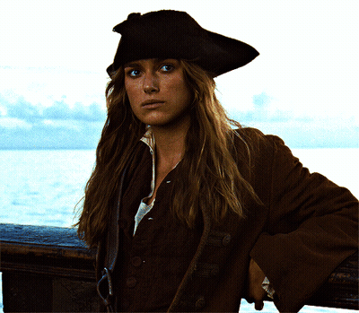 A Woman Wearing A Pirate Hat And A Brown Coat Leans On A Railing Overlooking The Ocean GIF