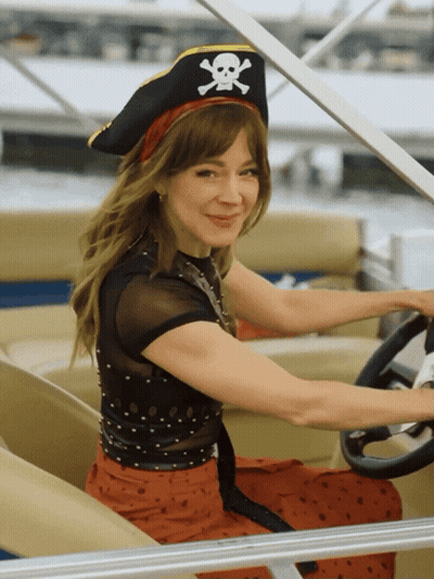 A Woman Wearing A Pirate Hat With A Skull And Crossbones On It Is Driving A Boat GIF
