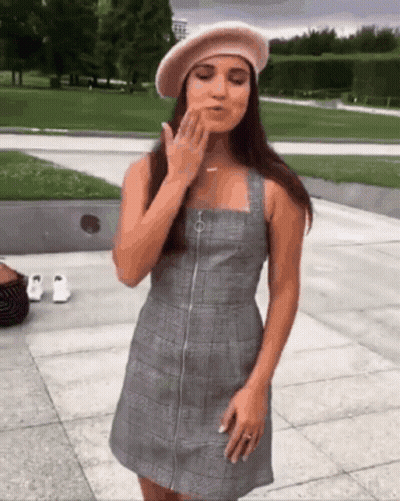 A Woman Wearing A Plaid Dress And A Beret Blows A Kiss GIF