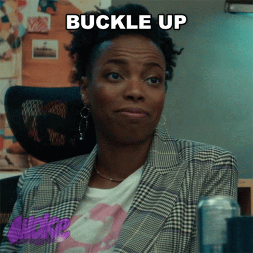 A Woman Wearing A Plaid Jacket And A T-Shirt That Says Buckle Up GIF