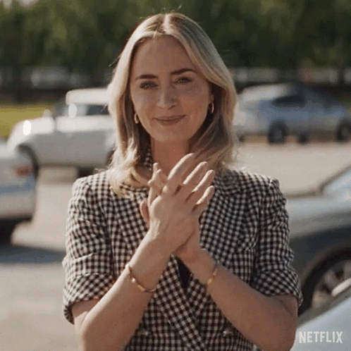 A Woman Wearing A Plaid Jacket Is Clapping Her Hands In A Parking Lot . GIF