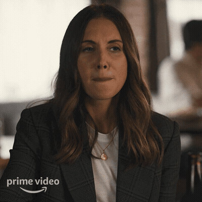 A Woman Wearing A Plaid Jacket Is Sitting In Front Of A Prime Video Ad GIF