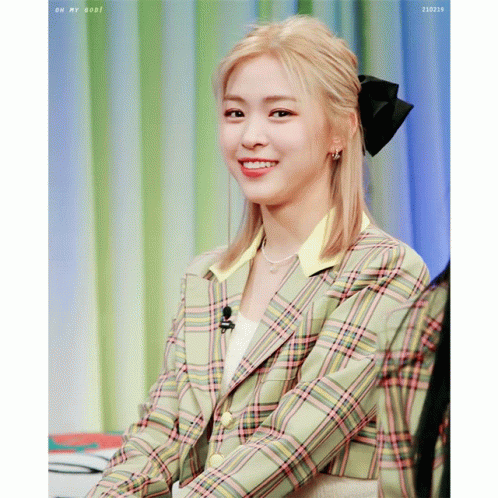 A Woman Wearing A Plaid Jacket With A Bow In Her Hair Smiles GIF