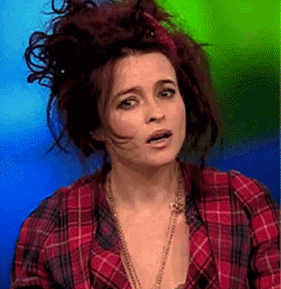 A Woman Wearing A Plaid Shirt And A Necklace Is Making A Funny Face GIF