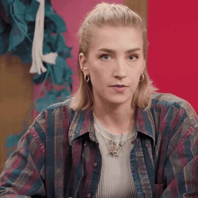 A Woman Wearing A Plaid Shirt And A Necklace With A Pendant That Says ' A ' On It GIF