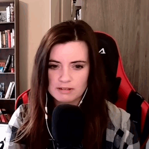 A Woman Wearing A Plaid Shirt Is Sitting In Front Of A Microphone With The Letter A On Her Back GIF