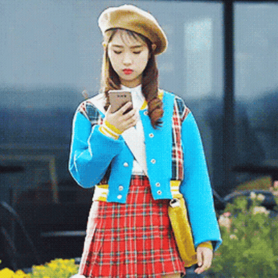 A Woman Wearing A Plaid Skirt And A Beret Looks At Her Phone GIF