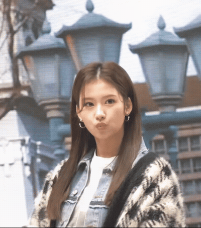 A Woman Wearing A Plaid Sweater And A Denim Jacket Is Standing In Front Of Street Lights GIF