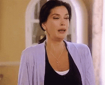 A Woman Wearing A Purple Cardigan And A Black Shirt Is Standing In A Room . GIF