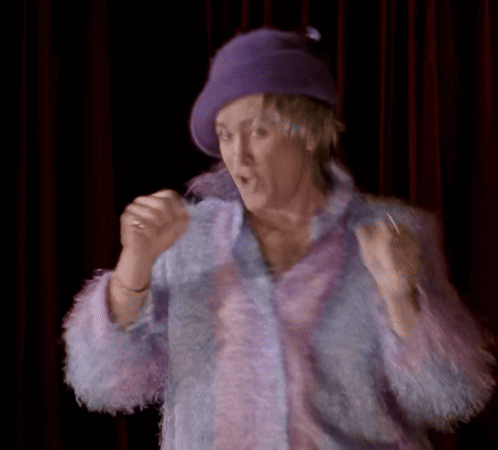 A Woman Wearing A Purple Hat And A Purple Coat Is Making A Funny Face GIF