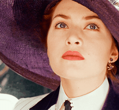 A Woman Wearing A Purple Hat And Earrings Looks Up At Something GIF