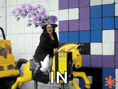 A Woman Wearing A Purple Hat Is Riding A Carousel Horse . GIF