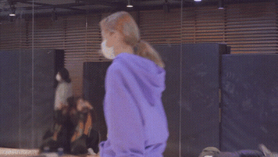 A Woman Wearing A Purple Hoodie And A Bandana Is Standing In A Room . GIF