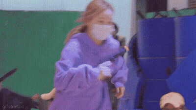 A Woman Wearing A Purple Hoodie And A White Mask Is Holding A Toy . GIF
