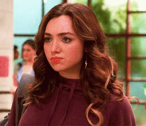 A Woman Wearing A Purple Hoodie And Earrings With A Lightning Bolt On Them Is Looking At The Camera . GIF