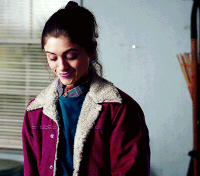 A Woman Wearing A Purple Jacket And A Plaid Shirt Smiles GIF