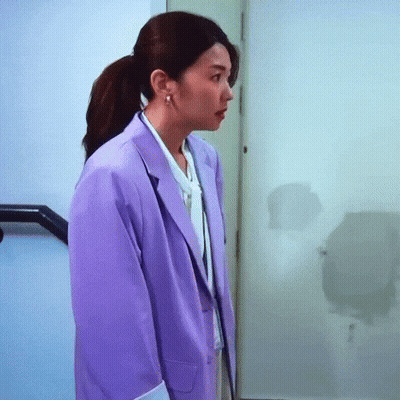 A Woman Wearing A Purple Jacket And A White Shirt Is Standing In A Hallway . GIF