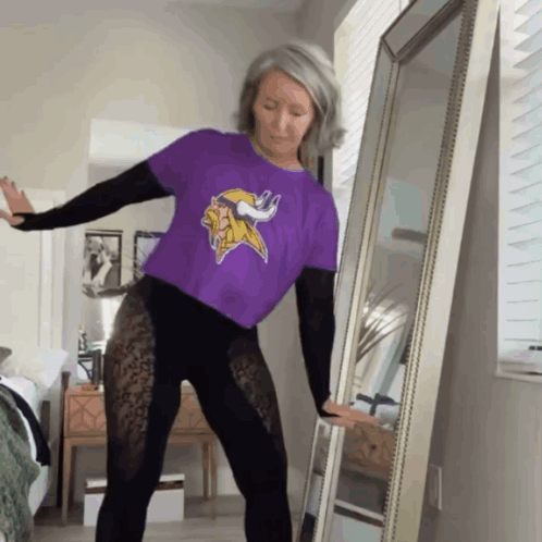 A Woman Wearing A Purple Minnesota Vikings Shirt Is Dancing In Front Of A Mirror GIF