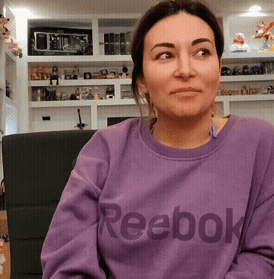A Woman Wearing A Purple Reebok Sweatshirt Looks At The Camera GIF