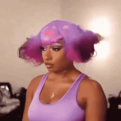 A Woman Wearing A Purple Tank Top And A Purple Wig Is Standing In A Room . GIF