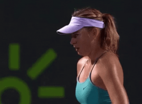 A Woman Wearing A Purple Visor And A Blue Tank Top Is Playing Tennis On A Court . GIF