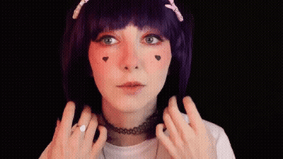 A Woman Wearing A Purple Wig And A Choker Is Smiling And Making A Peace Sign . GIF