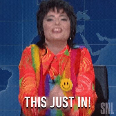 A Woman Wearing A Rainbow Shirt And A Smiley Face Necklace Says This Just In GIF