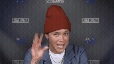 A Woman Wearing A Red Beanie Is Smiling In Front Of A Wall With The Word Challenge On It GIF