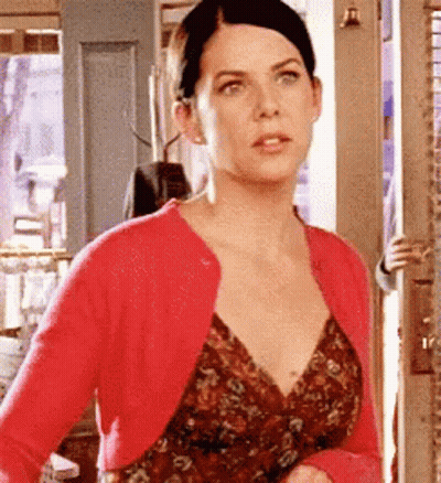 A Woman Wearing A Red Cardigan And A Floral Dress Is Standing In A Doorway . GIF