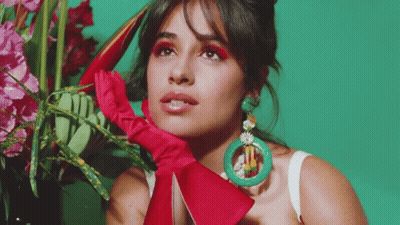 A Woman Wearing A Red Glove And Green Earrings Is Standing In Front Of A Vase Of Flowers GIF