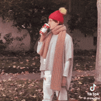 A Woman Wearing A Red Hat And Scarf Is Drinking A Cup Of Coffee GIF