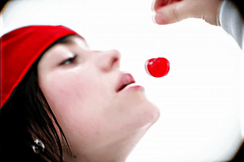 A Woman Wearing A Red Hat Is Eating A Red Candy GIF