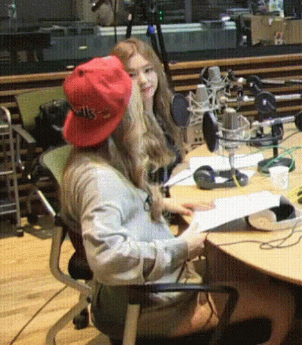 A Woman Wearing A Red Hat That Says Wks Sits At A Desk GIF