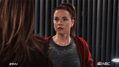 A Woman Wearing A Red Hoodie Is Sitting In Front Of A Curtain With Nbc Written On It GIF