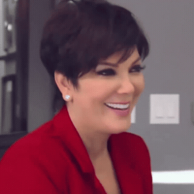 A Woman Wearing A Red Jacket And Earrings Is Smiling And Looking At The Camera . GIF