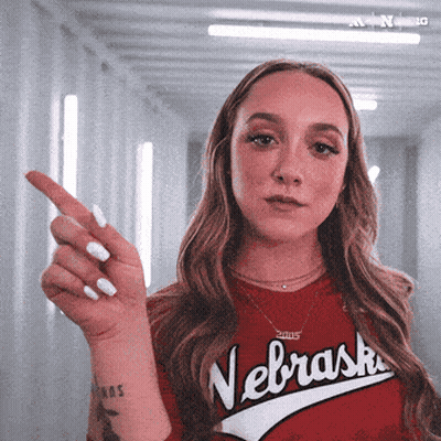 A Woman Wearing A Red Nebraska Shirt Is Pointing At Something GIF