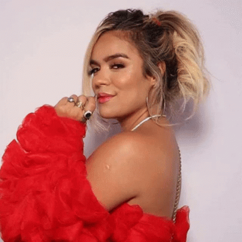 A Woman Wearing A Red Ruffled Sleeved Top Is Looking Over Her Shoulder At The Camera GIF