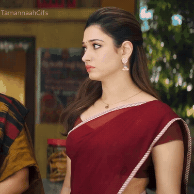 A Woman Wearing A Red Saree And Earrings Stands In Front Of A Sign That Says " Tamannahgifs " GIF