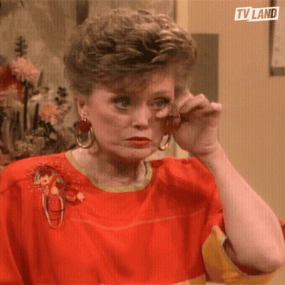 A Woman Wearing A Red Shirt And Earrings Wipes Her Eyes With Her Hand .. GIF